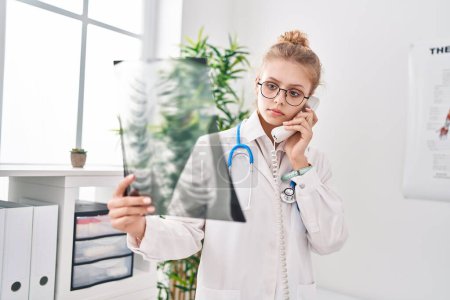 Photo for Young blonde woman doctor talking on telephone holding xray at clinic - Royalty Free Image