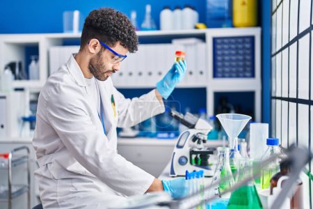 Téléchargez les photos : Jeune homme arabe portant un uniforme de scientifique tenant une éprouvette d'urine au laboratoire - en image libre de droit