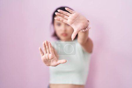 Photo for Hispanic young woman standing over pink background doing frame using hands palms and fingers, camera perspective - Royalty Free Image