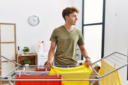 Téléchargez les photos : Young caucasian man smiling confident hanging clothes at laundry room - en image libre de droit