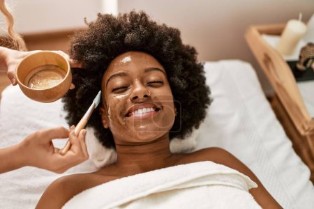 Téléchargez les photos : Jeune femme afro-américaine souriante confiante ayant un traitement du visage au centre de beauté - en image libre de droit