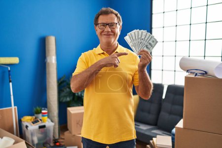 Téléchargez les photos : Homme âgé déménageant dans une nouvelle maison tenant de l'argent souriant heureux pointant avec la main et le doigt - en image libre de droit