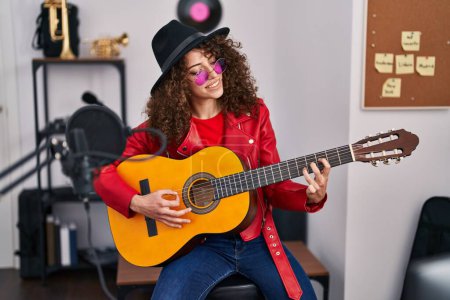 Photo for Young hispanic woman musician singing song playing classical guitar at music studio - Royalty Free Image