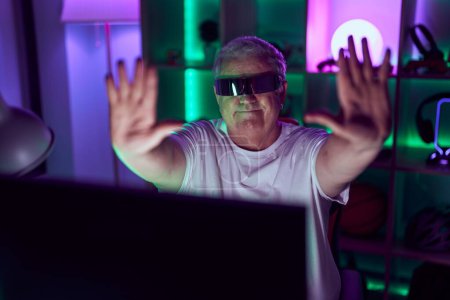 Photo for Middle age grey-haired man streamer playing video game using virtual reality glasses at gaming room - Royalty Free Image