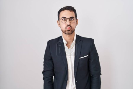Foto de Handsome business hispanic man standing over white background puffing cheeks with funny face. mouth inflated with air, crazy expression. - Imagen libre de derechos