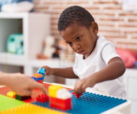 Foto de Niño afroamericano jugando con bloques de construcción sentado en la mesa en el jardín de infantes - Imagen libre de derechos
