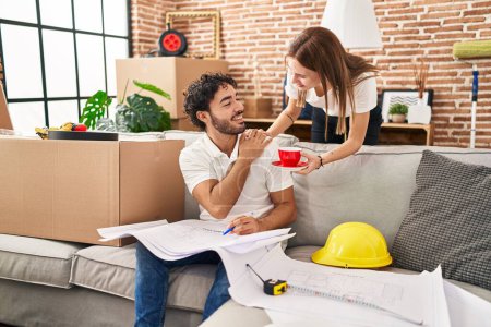 Photo for Man and woman couple drinking coffee looking house plans at new home - Royalty Free Image