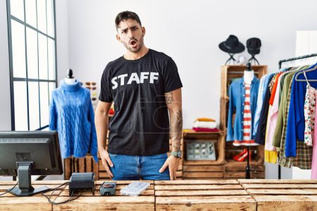 Photo for Young hispanic man working at retail boutique in shock face, looking skeptical and sarcastic, surprised with open mouth - Royalty Free Image