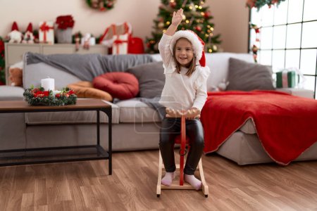 Photo for Adorable hispanic girl playing with reindeer rocking by christmas tree at home - Royalty Free Image