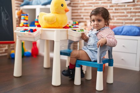 Foto de Adorable chica hispana jugando con bloques de construcción sentada en la mesa en el jardín de infantes - Imagen libre de derechos