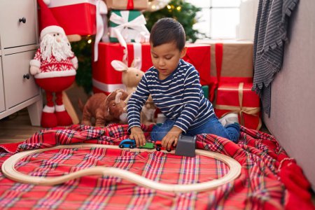 Foto de Adorable niño hispano jugando con el juguete del coche sentado en el suelo por el árbol de Navidad en casa - Imagen libre de derechos