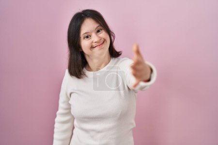 Téléchargez les photos : Femme avec le syndrome du duvet debout sur fond rose souriant amical offrant poignée de main comme salutation et accueil. entreprise prospère. - en image libre de droit