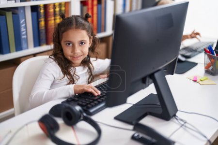 Photo for Adorable hispanic girl student using computer sitting on table at classroom - Royalty Free Image