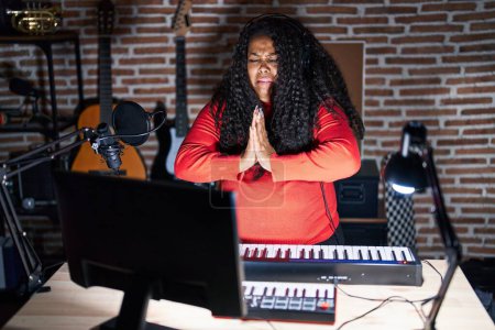 Téléchargez les photos : Plus taille hispanique femme jouant du piano au studio de musique mendier et prier avec les mains ainsi que l'expression de l'espoir sur le visage très émotionnel et inquiet. mendier. - en image libre de droit