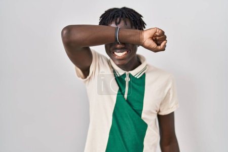 Foto de African man with dreadlocks standing over isolated background covering eyes with arm smiling cheerful and funny. blind concept. - Imagen libre de derechos