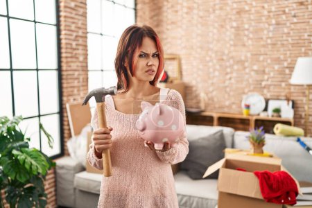 Photo for Young caucasian woman holding piggy bank at new home clueless and confused expression. doubt concept. - Royalty Free Image