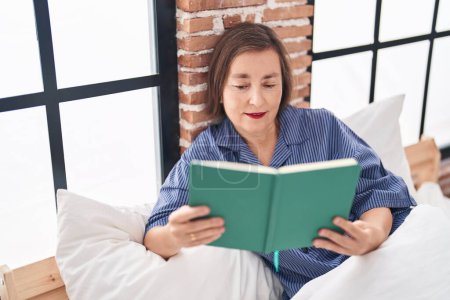 Téléchargez les photos : Moyen âge femme lecture livre assis sur le lit à la chambre - en image libre de droit