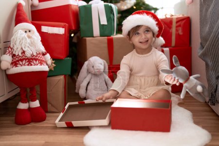Photo for Adorable girl unpacking gift sitting by christmas tree at home - Royalty Free Image