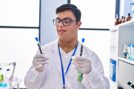 Téléchargez les photos : Homme trisomique portant un uniforme scientifique tenant des éprouvettes en laboratoire - en image libre de droit