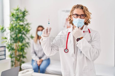 Photo for Blond man wearing doctor uniform and medical mask holding syringe serious face thinking about question with hand on chin, thoughtful about confusing idea - Royalty Free Image