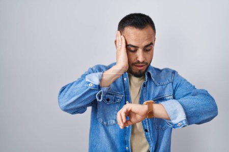 Téléchargez les photos : Jeune homme hispanique debout sur fond isolé regardant le temps de la montre inquiet, peur de se faire tard - en image libre de droit