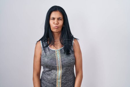 Photo for Mature hispanic woman standing over white background puffing cheeks with funny face. mouth inflated with air, crazy expression. - Royalty Free Image