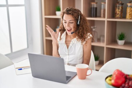 Foto de Young caucasian woman wearing call center agent headset working from home screaming proud, celebrating victory and success very excited with raised arm - Imagen libre de derechos