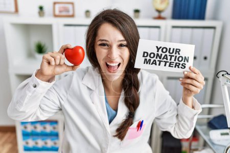 Téléchargez les photos : Jeune femme médecin tenant votre bannière de questions de don à la clinique souriant et riant fort à haute voix parce que drôle blague folle. - en image libre de droit