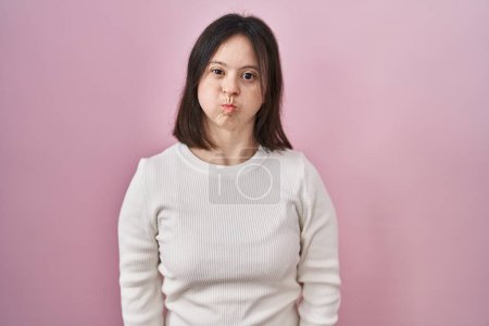 Photo for Woman with down syndrome standing over pink background puffing cheeks with funny face. mouth inflated with air, crazy expression. - Royalty Free Image