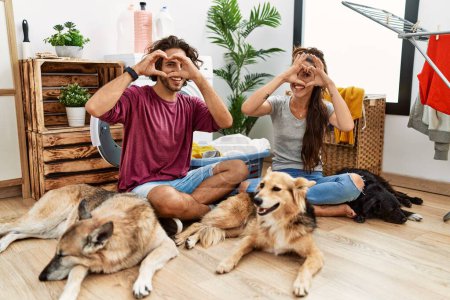 Photo for Young hispanic couple doing laundry with dogs doing heart shape with hand and fingers smiling looking through sign - Royalty Free Image