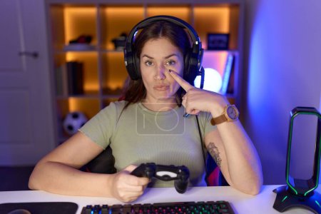 Photo for Beautiful brunette woman playing video games wearing headphones pointing to the eye watching you gesture, suspicious expression - Royalty Free Image