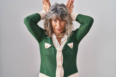 Photo for Middle age woman standing over white background doing bunny ears gesture with hands palms looking cynical and skeptical. easter rabbit concept. - Royalty Free Image