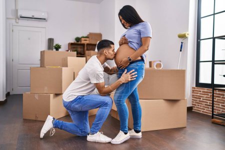 Photo for Young latin couple expecting baby kissing tummy at new home - Royalty Free Image