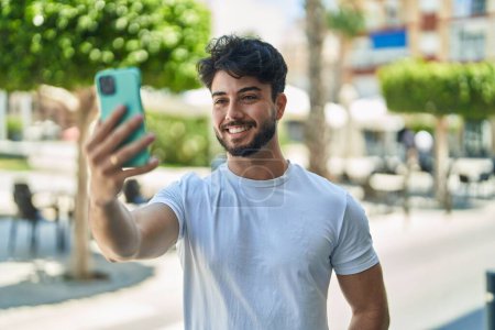 Photo for Young hispanic man smiling confident making selfie by the smartphone at street - Royalty Free Image