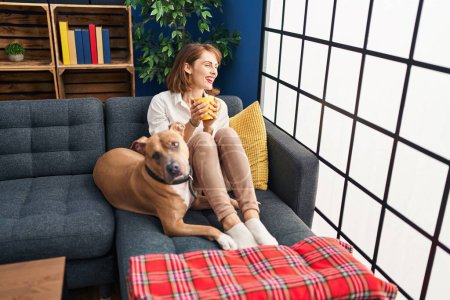 Téléchargez les photos : Jeune femme caucasienne buvant du café assis sur un canapé avec chien à la maison - en image libre de droit