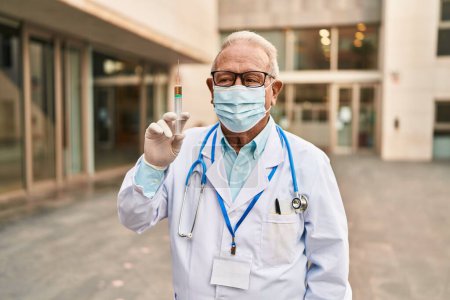 Photo for Senior doctor with grey hair wearing safety mask holding syringe looking positive and happy standing and smiling with a confident smile showing teeth - Royalty Free Image