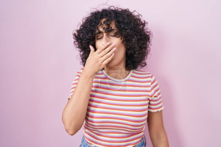 Téléchargez les photos : Young middle east woman standing over pink background bored yawning tired covering mouth with hand. restless and sleepiness. - en image libre de droit