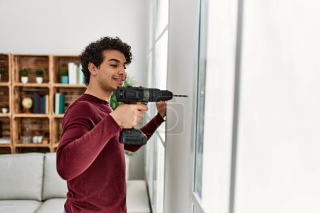 Photo for Young hispanic man smiling happy drillling wall at home. - Royalty Free Image