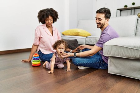 Foto de Pareja e hija sonriendo confiadas jugando con juguetes sentadas en el suelo en casa - Imagen libre de derechos
