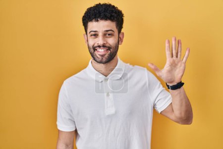 Téléchargez les photos : Arabe debout sur fond jaune montrant et pointant vers le haut avec les doigts numéro cinq tout en souriant confiant et heureux. - en image libre de droit