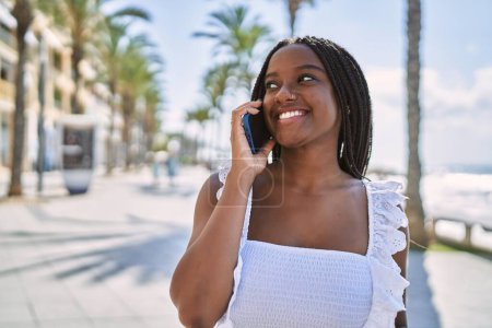 Téléchargez les photos : Jeune fille afro-américaine souriante heureuse de parler sur le smartphone à la promenade. - en image libre de droit