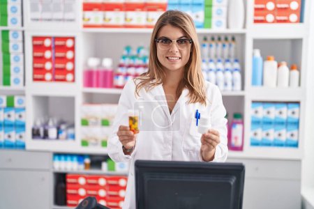 Foto de Young woman pharmacist smiling confident holding pills bottles at pharmacy - Imagen libre de derechos