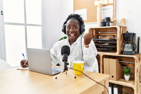 Téléchargez les photos : Jeune femme africaine travaillant au studio de radio criant fier, célébrant la victoire et le succès très excité avec les bras levés - en image libre de droit