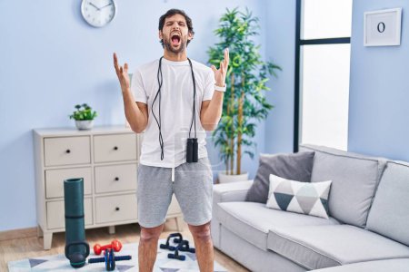 Photo for Handsome latin man wearing sportswear at home crazy and mad shouting and yelling with aggressive expression and arms raised. frustration concept. - Royalty Free Image