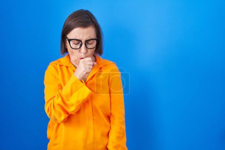 Photo for Middle age hispanic woman wearing glasses standing over blue background feeling unwell and coughing as symptom for cold or bronchitis. health care concept. - Royalty Free Image