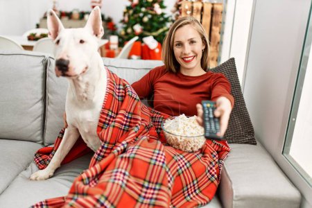 Foto de Joven mujer caucásica viendo la película sentado con el perro por el árbol de Navidad en casa - Imagen libre de derechos