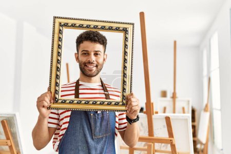 Photo for Young arab artist man smiling happy holding empty frame at art studio. - Royalty Free Image