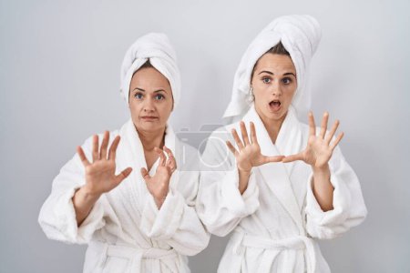 Photo for Middle age woman and daughter wearing white bathrobe and towel afraid and terrified with fear expression stop gesture with hands, shouting in shock. panic concept. - Royalty Free Image