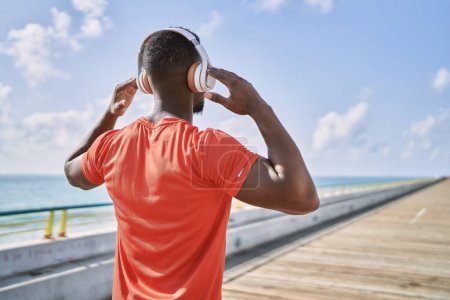 Téléchargez les photos : Jeune homme afro-américain écoutant de la musique au bord de la mer - en image libre de droit