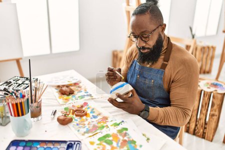 Téléchargez les photos : Jeune artiste afro-américain concentré peinture céramique au studio d'art. - en image libre de droit